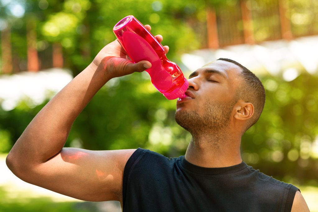man drinking water from red sports bottle after sweaty workout
